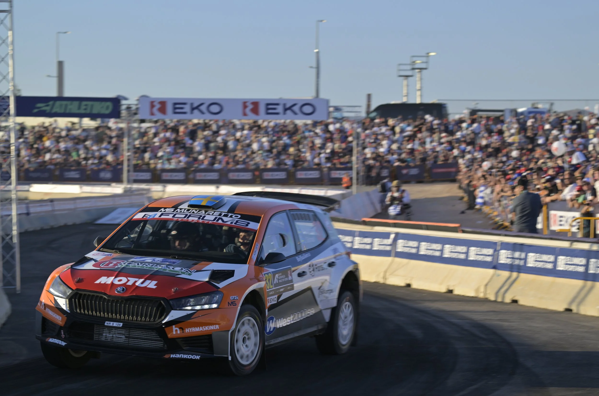 Race car speeding on a track with a large crowd of spectators in the background.