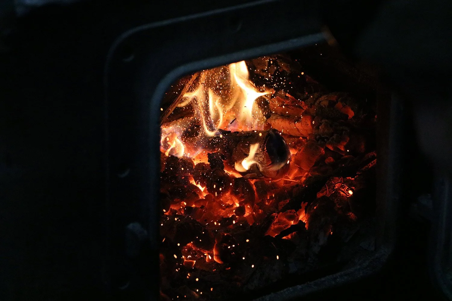 Fire burning inside a metal stove with glowing embers and flames.