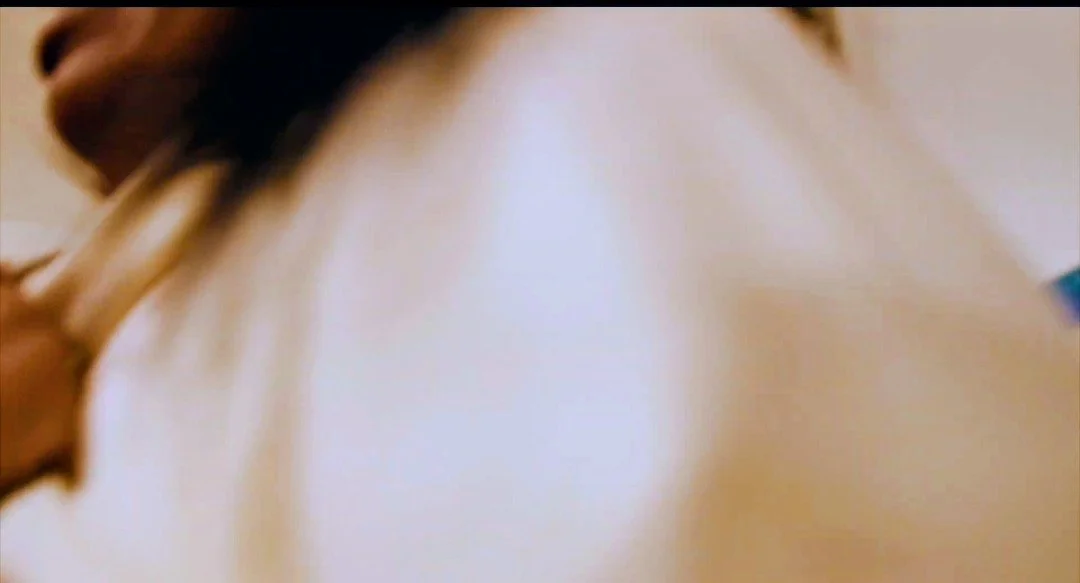 Close-up of a person's face and shoulder, with a focus on their mouth and hair, in a blurred background.