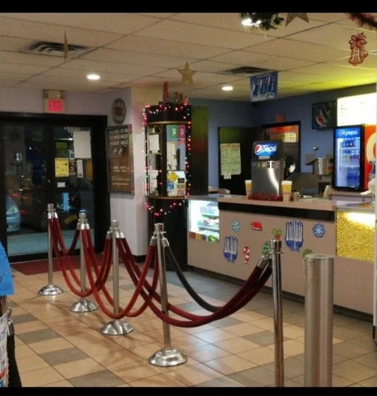 Inside a fast-food restaurant or soda fountain with a counter, beverage dispensers, and Christmas decorations, including red and gold garlands and ornaments, and festive stickers on the counter.