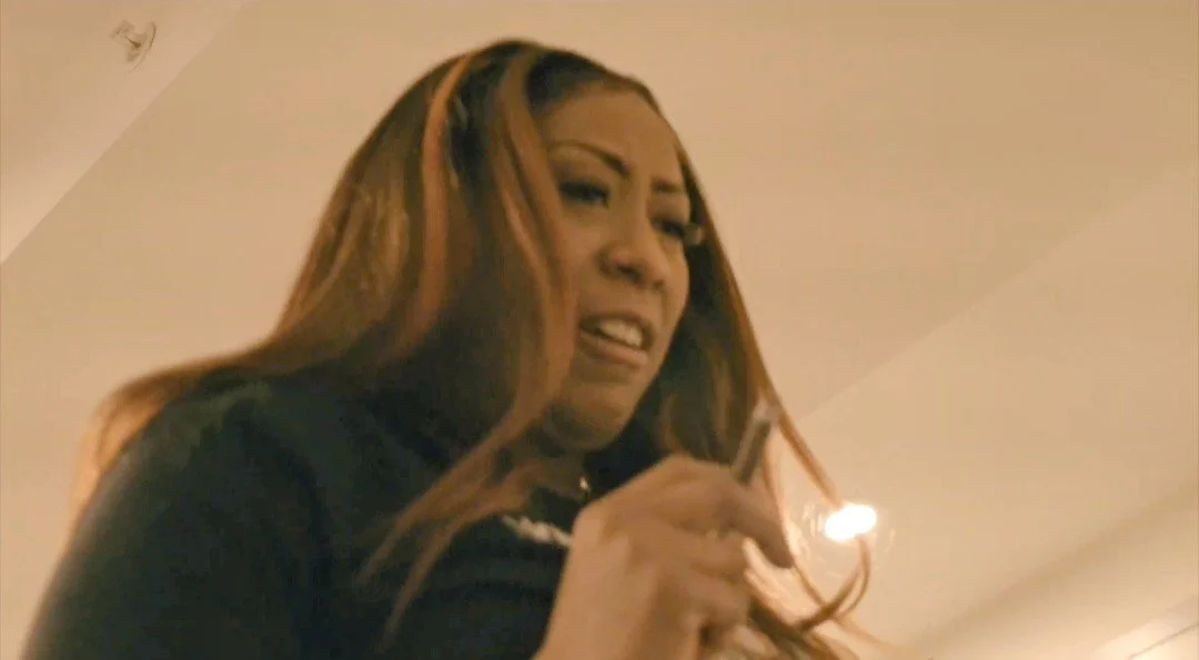 A woman with long, highlighted hair making a humorous facial expression while holding a phone.