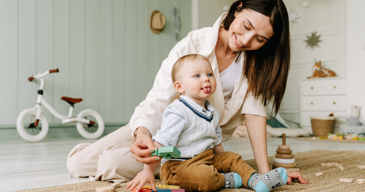 A woman and a young child playing on the floor in a child's room, with a bicycle in the background.