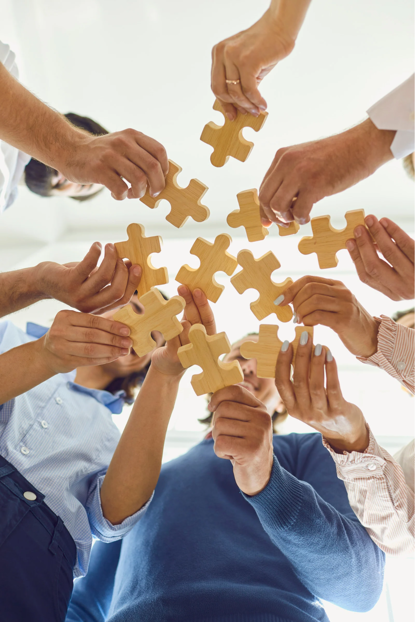 Multiple people holding and connecting wooden puzzle pieces together.