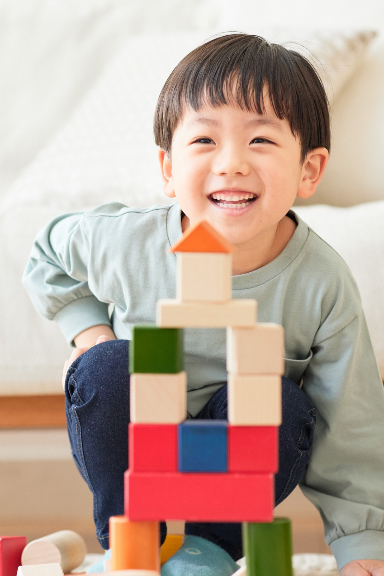 A young boy with a happy expression playing with colorful wooden building blocks.