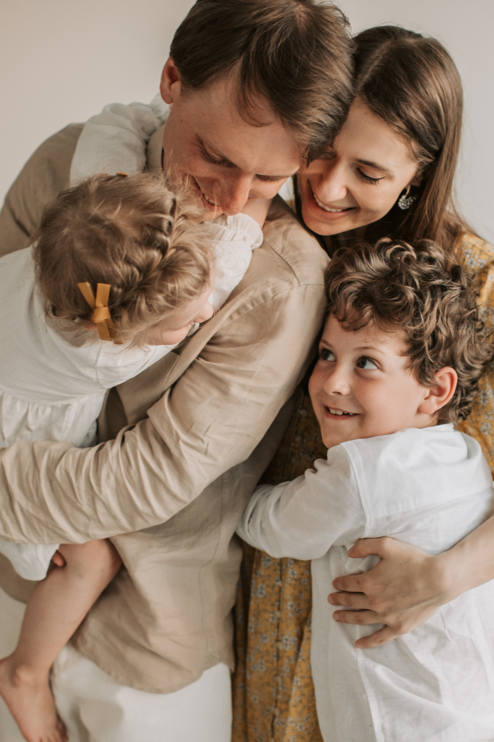 A family group hug with two adults and three children, all smiling and embracing each other in a warm, affectionate moment.