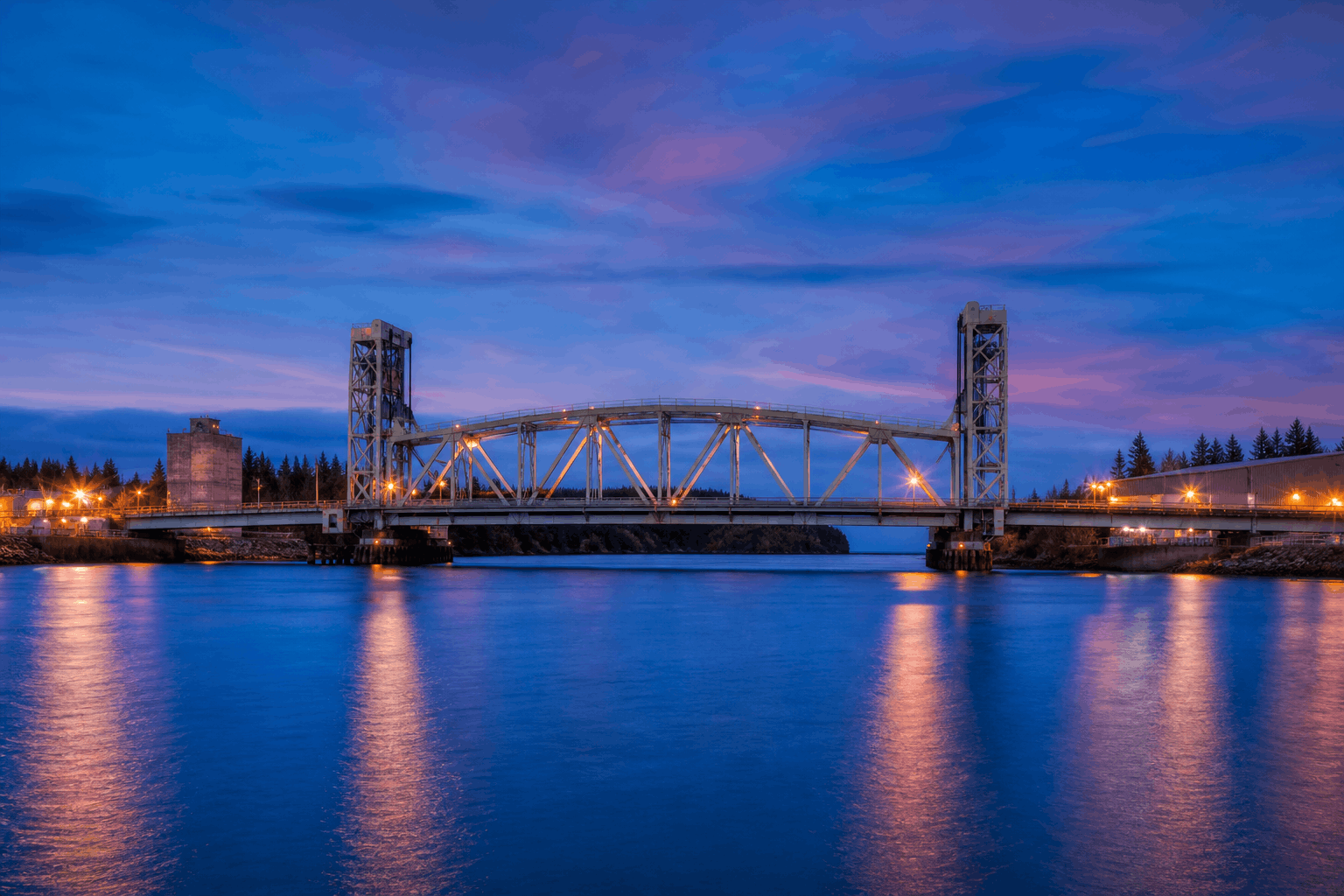 Operational steel bridge spanning an industrial waterway at blue hour