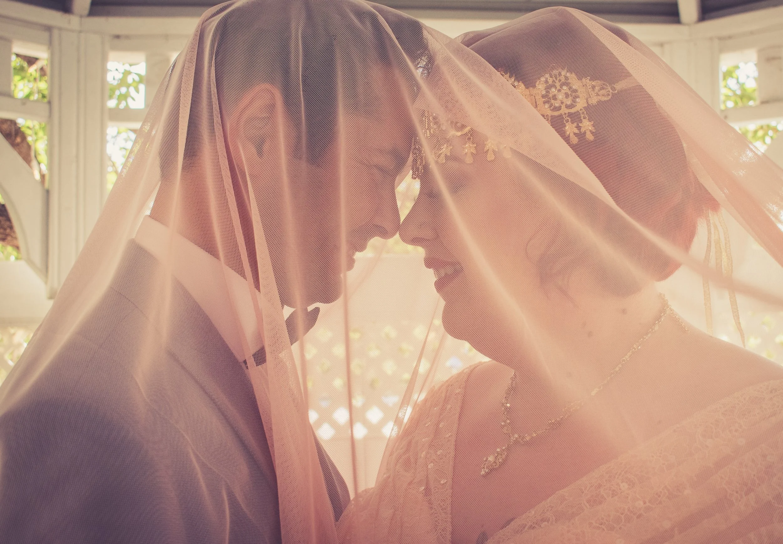 Two women with veils and jewelry touching foreheads in an intimate moment.