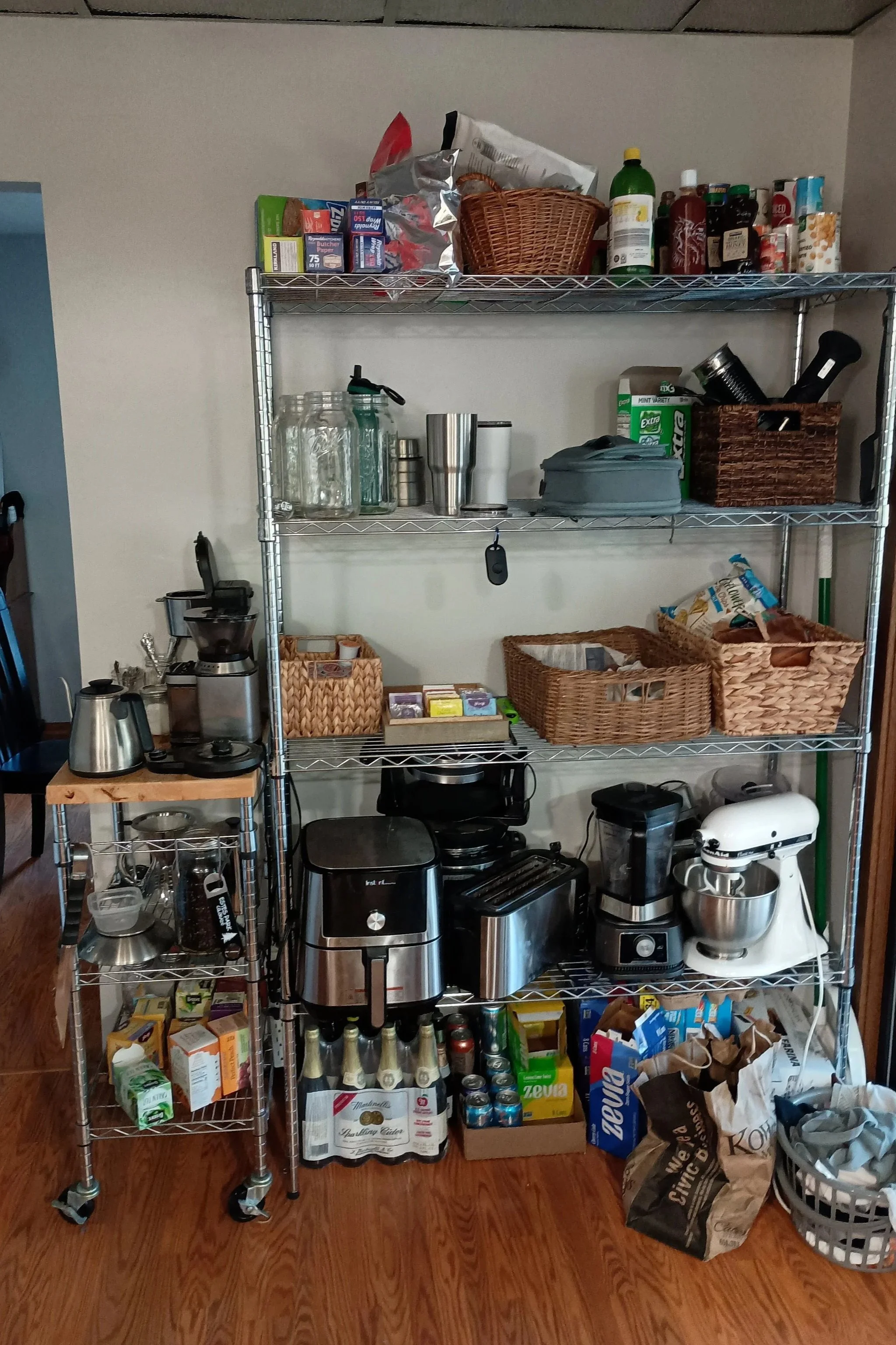 Pantry shelves filled with various food items, drinks, and kitchen appliances, with boxes of cereal, bottles, jars, and pantry staples visible.