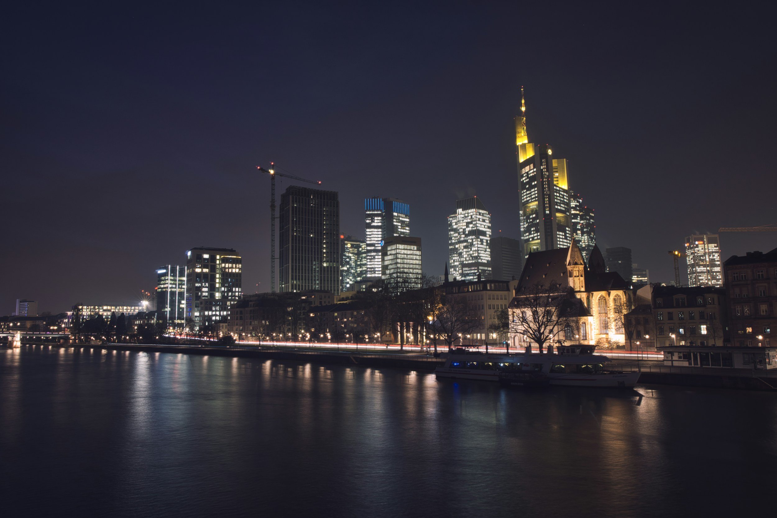 Stadt bei Nacht mit Hochhäusern, Kirchen und Wasser im Vordergrund.