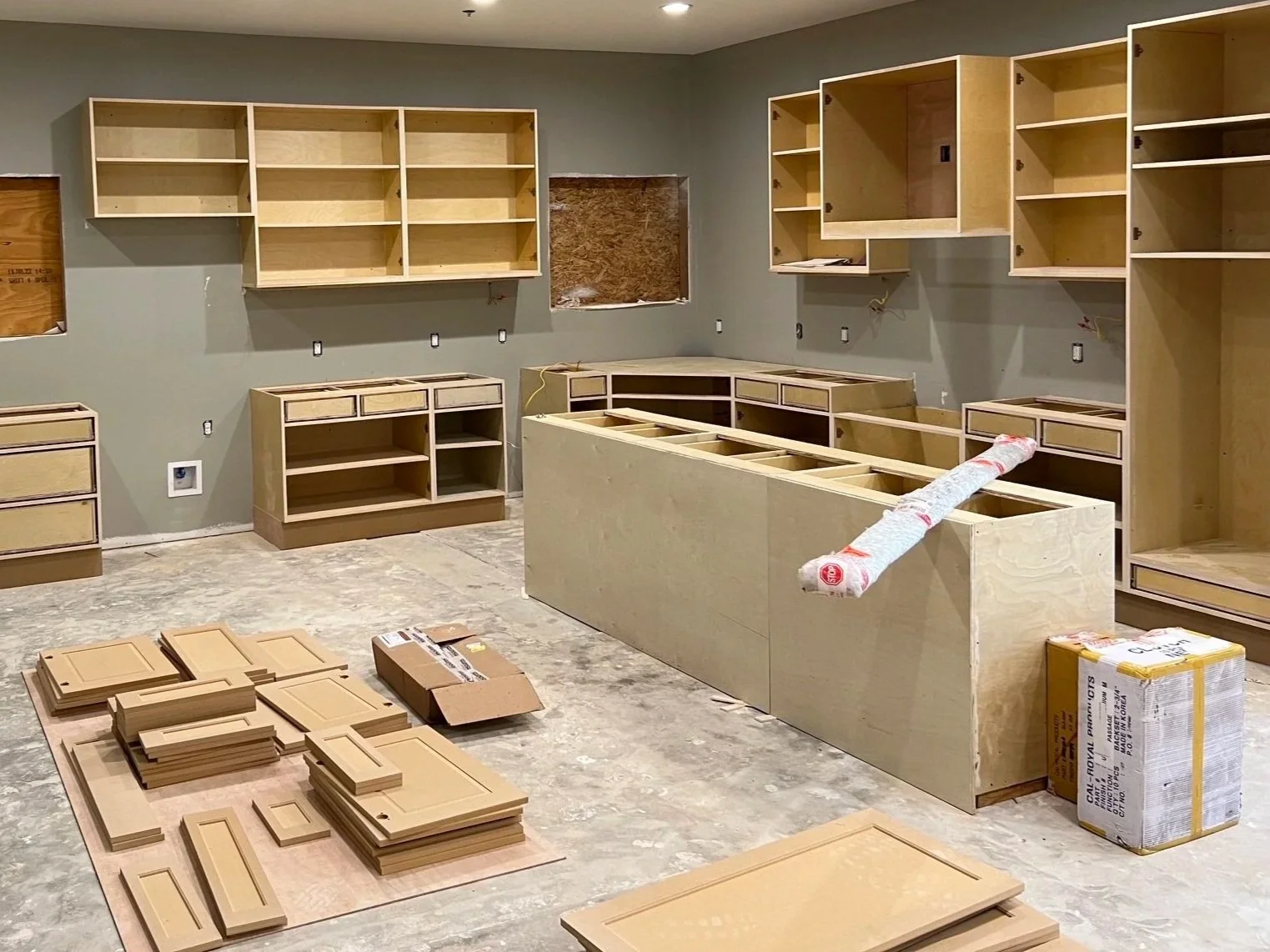A room under renovation with unfinished cabinets and shelves being installed. Construction materials and tools are scattered around.