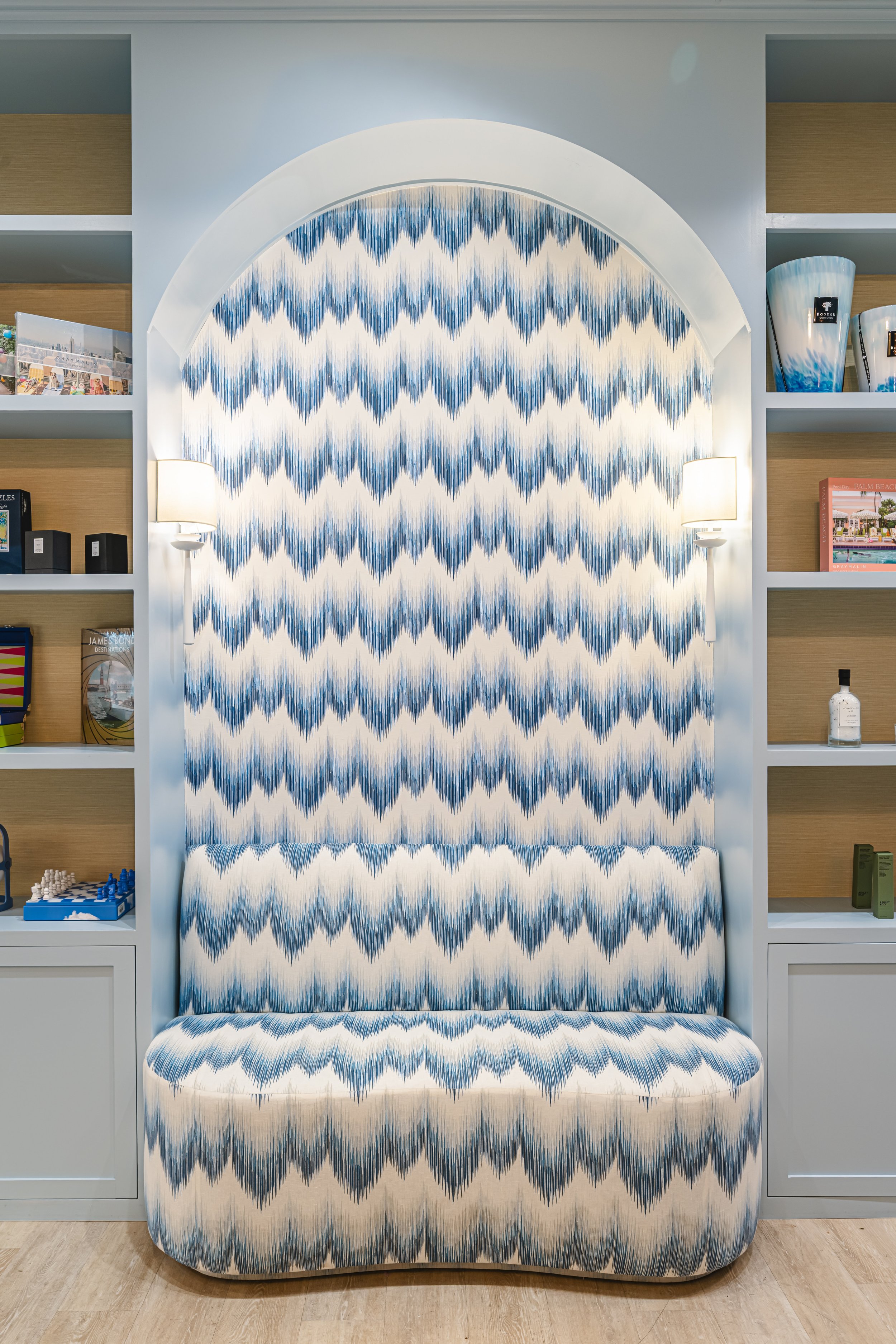 A chair with a blue, white, and black zigzag patterned fabric, located in front of a decorated wall with built-in bookshelves and two wall-mounted lamps.
