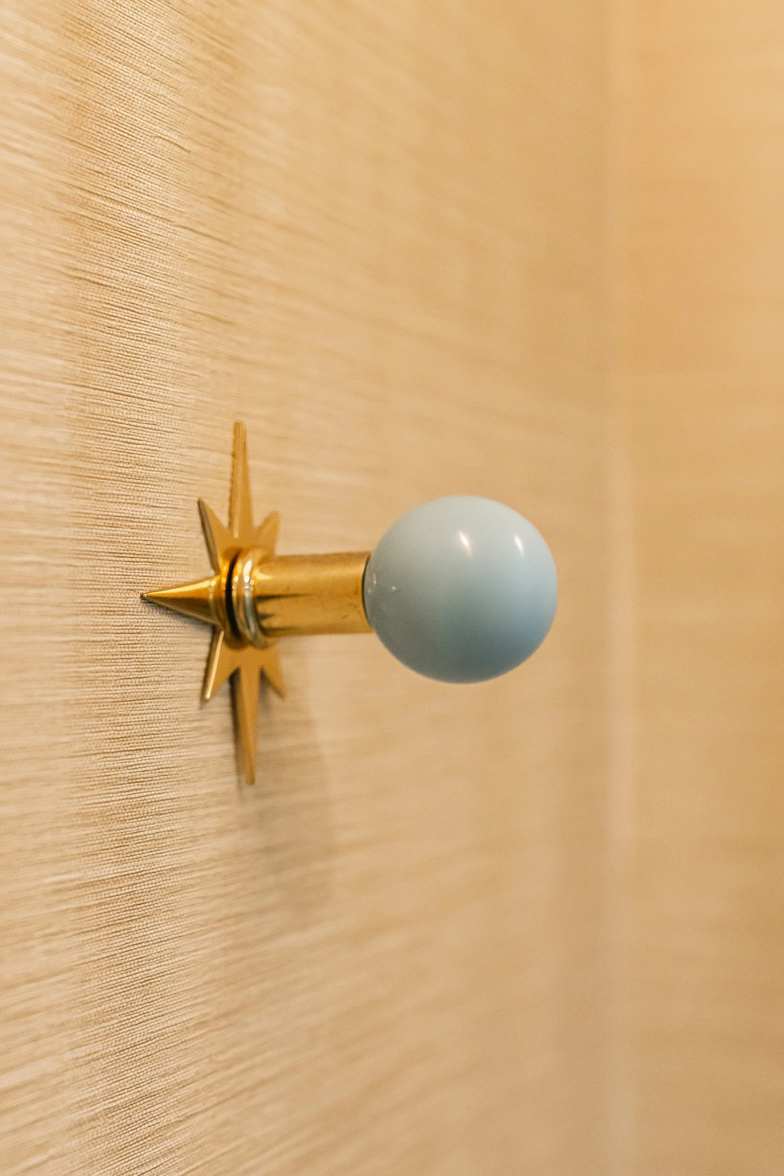 Decorative wall hook with a star design, gold and light blue colors, mounted on a wooden surface.