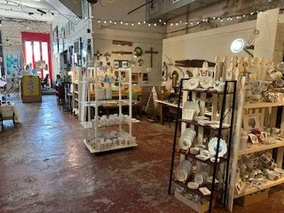 Interior of a decorative gift shop with shelves displaying various ceramics, plates, and decorative items, with a red door at the back.