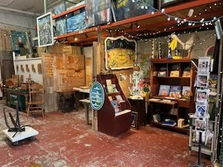 Indoor gift store with shelves and items, including a wooden bowls and cutting boards, ceramics and pottery, metal art and stain glass. Homemade journals and wood crafts. Paintings and sculptures too. Books, prints and gift items