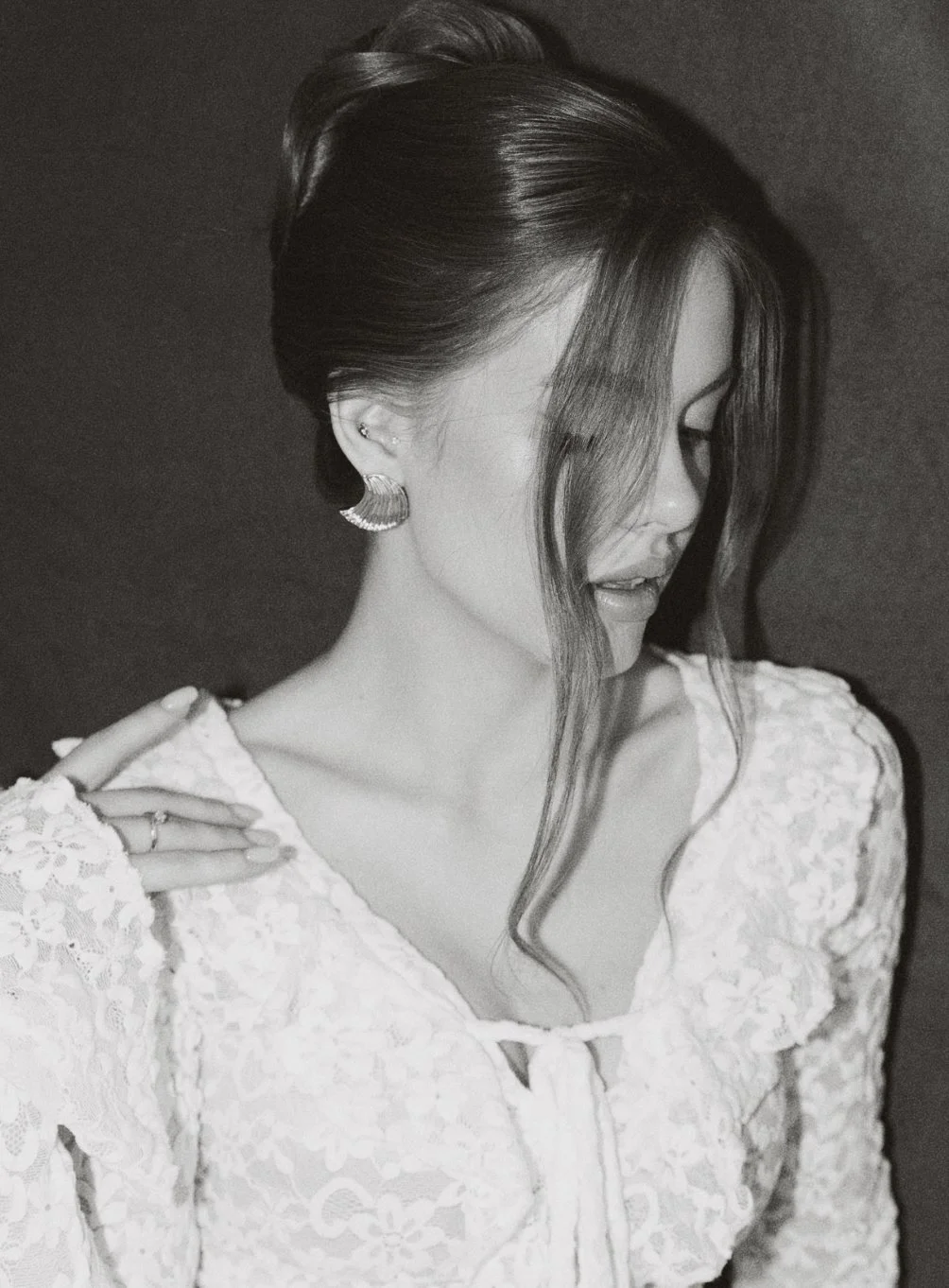 Portrait en noir et blanc d'une femme avec des cheveux longs et ondulés, portant un vêtement en dentelle et une boucle d'oreille élégante, regardant vers le bas.