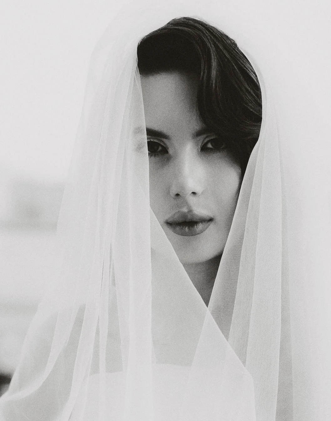 Portrait en noir et blanc d'une femme avec un voile semi-transparent, mettant en valeur ses yeux et ses lèvres.