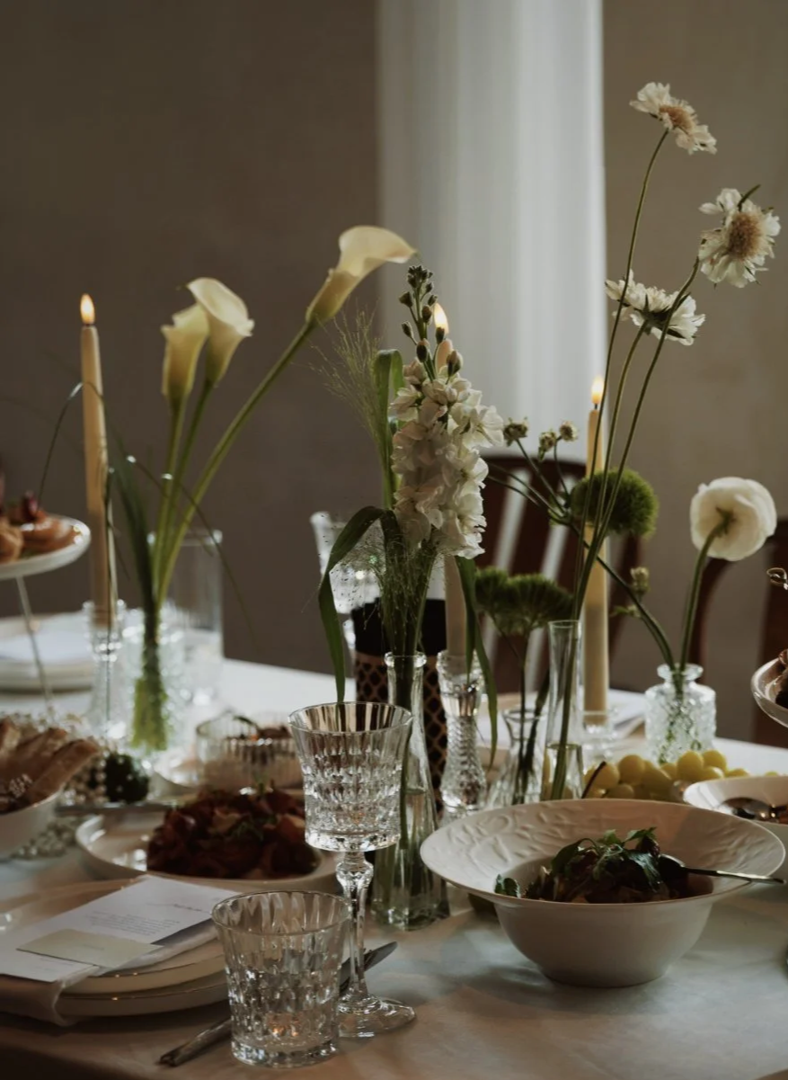 Table de dîner décorée avec des fleurs blanches, des bougies, des cristaux et des assiettes.