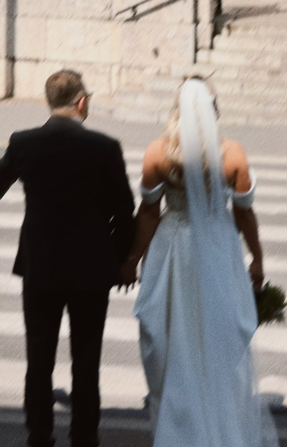 Un couple tenant la main devant un escalier en pierre, probablement lors d'un mariage.