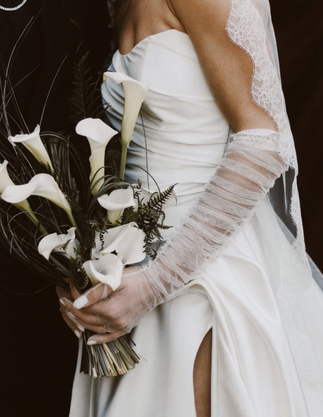 Femme en robe de mariée blanche tenant un bouquet de calla lilies avec des gants en dentelle