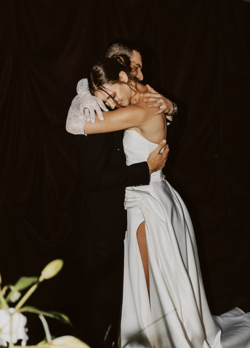 Deux personnes, en costume et robe de mariage, s'embrassent lors d'un mariage, dans un décor sombre.
