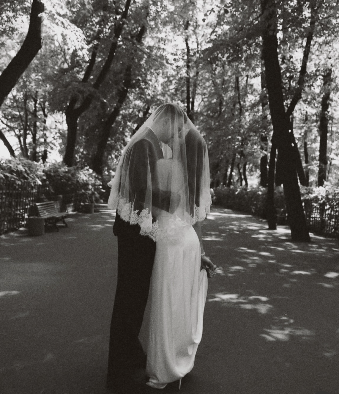 Un couple en mariage dans un parc, l'homme en costume noir, la femme en robe de mariée blanche avec voilette, au travers d'une lumière tamisée