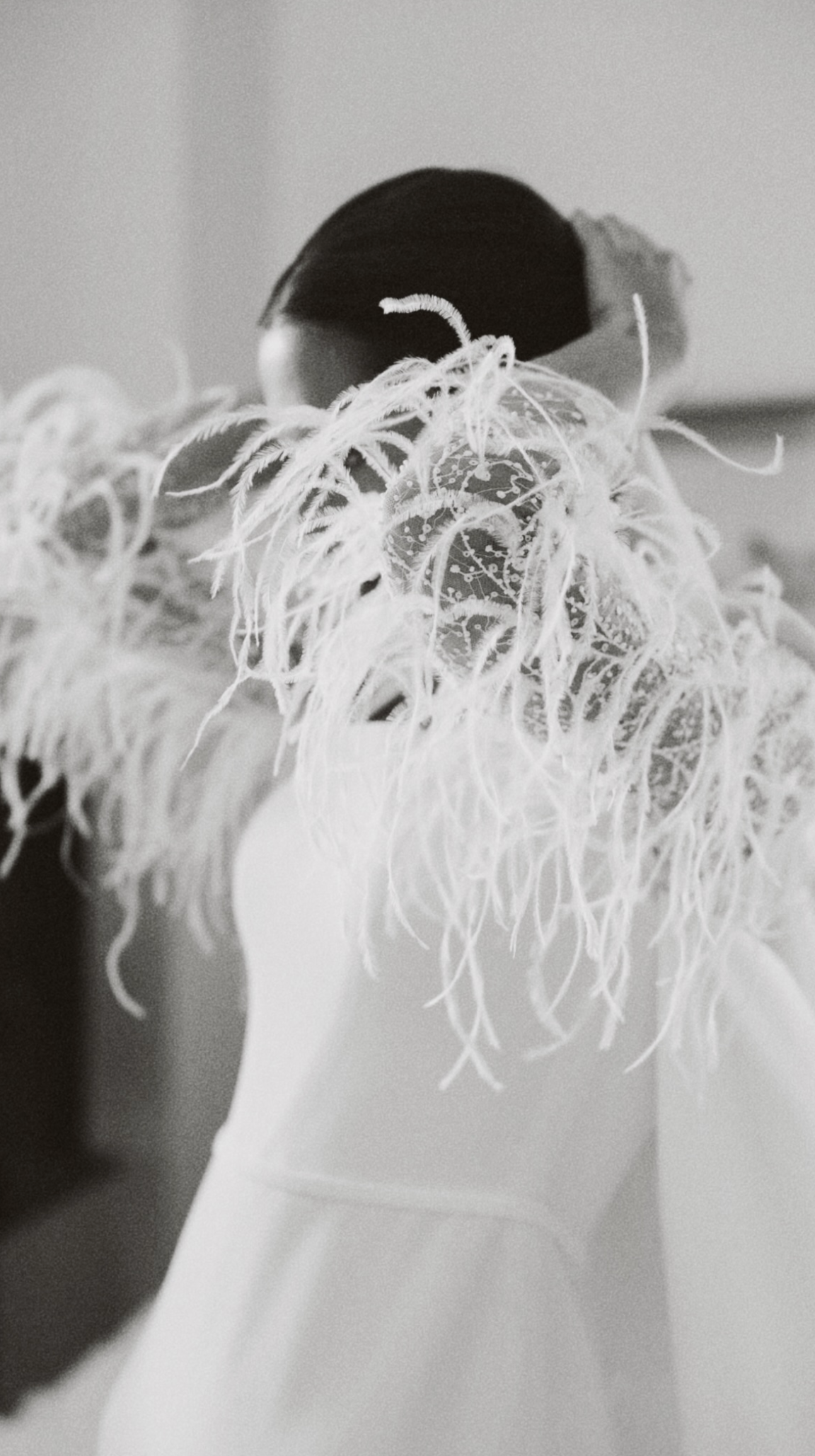 Une silhouette féminine avec un haut blanc sans manches, vu de dos, portant un objet composé de filaments délicats et ornementés.