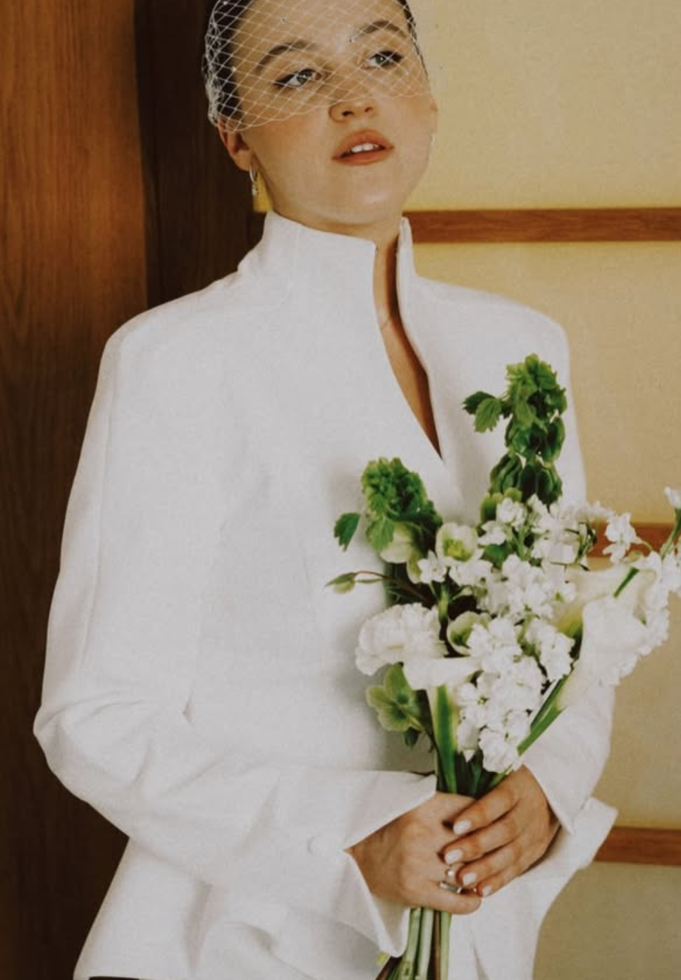 Femme portant une robe blanche, portant un voile en filet, tenant un bouquet de fleurs blanches et vertes.