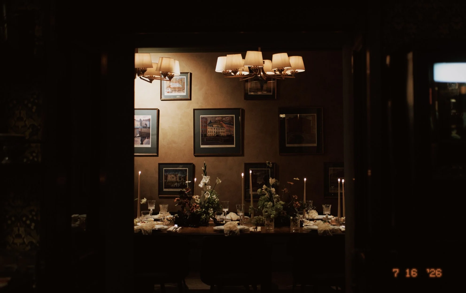 Une salle de dîner magnifiquement décorée avec un chandelier à plusieurs lampes, des tableaux accrochés au mur, et un arrangement floral au centre d'une table, à l'intérieur d'une pièce chaleureuse.