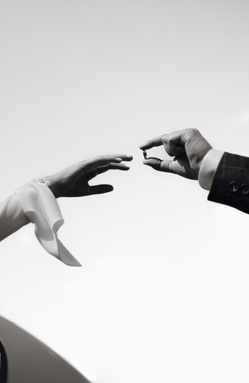 Deux mains, une d'homme en costume et une d'une femme avec un ruban blanc, échangeant un anneau lors d'une cérémonie.