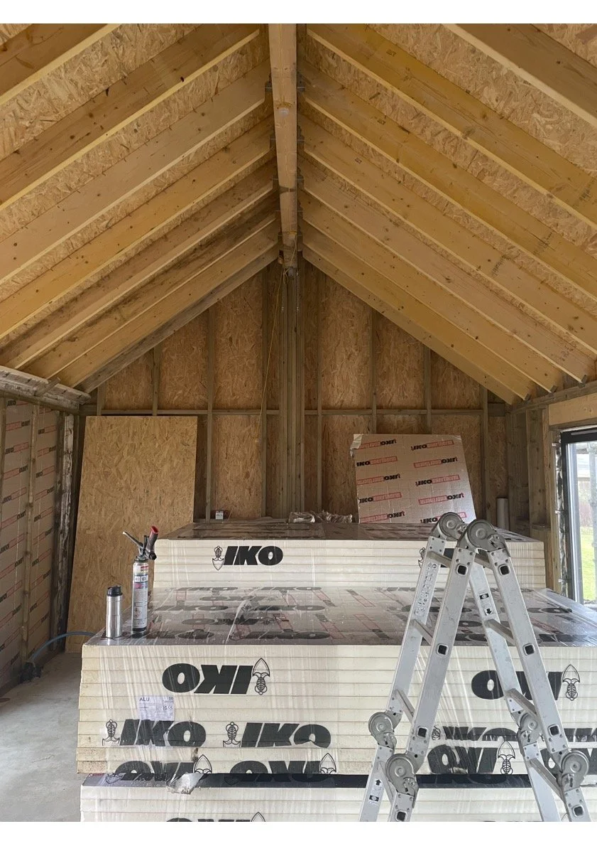 Interior of an unfinished attic or room under construction with exposed wooden framing, insulation boards, a ladder, and construction tools.
