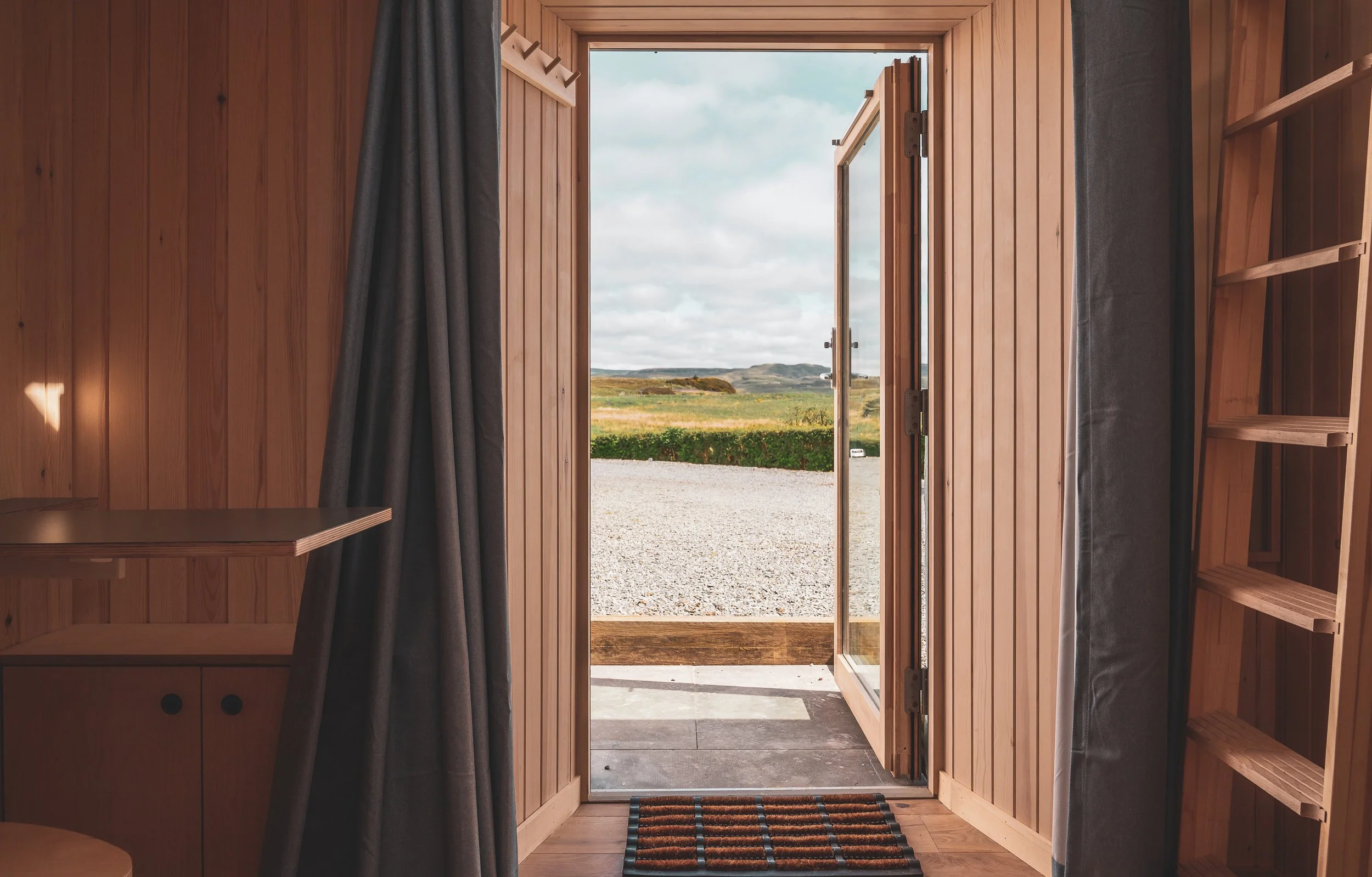Open wooden door leading outside to a scenic landscape with grassy fields and rolling hills sky with scattered clouds.