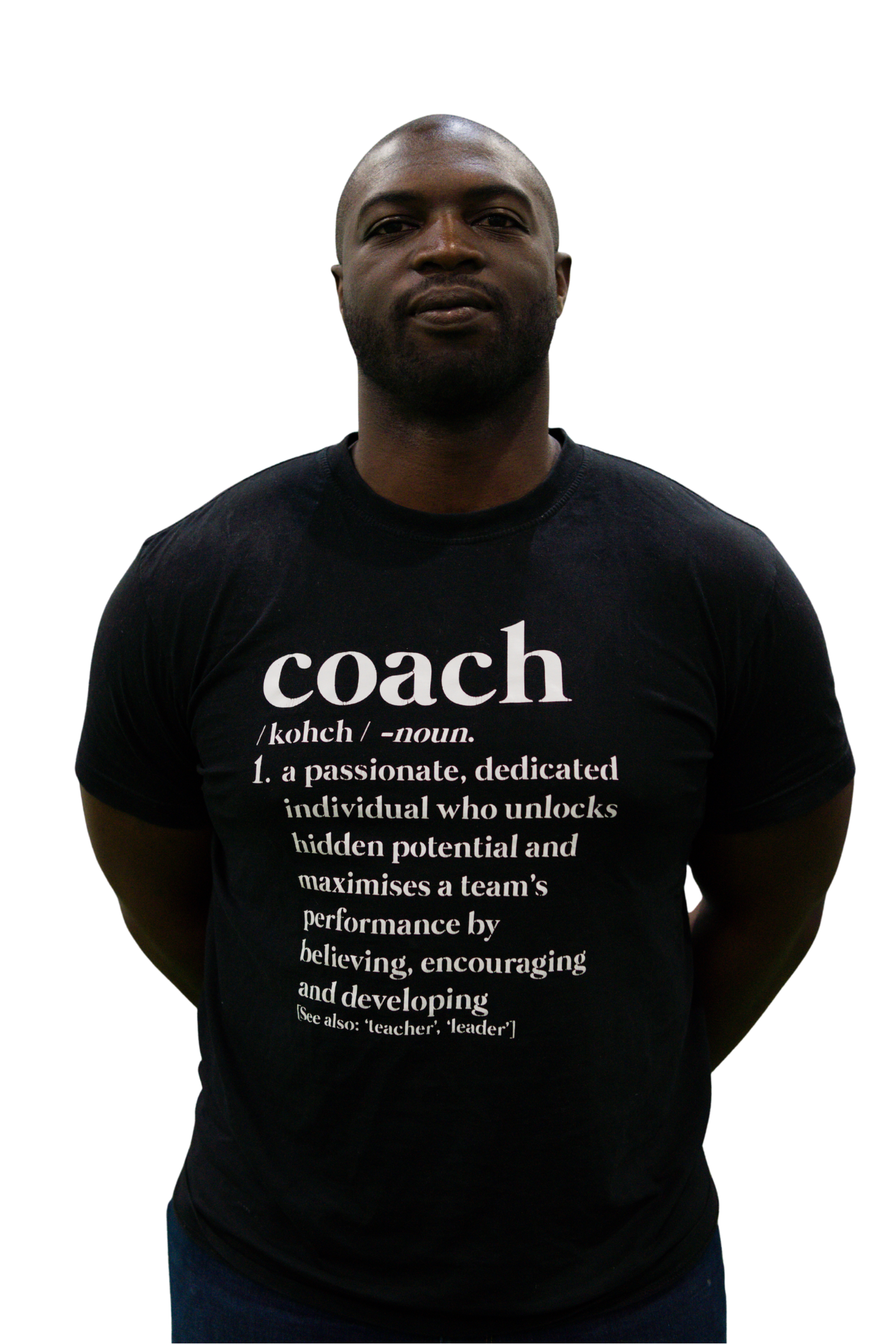 A man wearing a black T-shirt with the word 'coach' and its definition printed on it, standing with his hands behind his back against a black background.