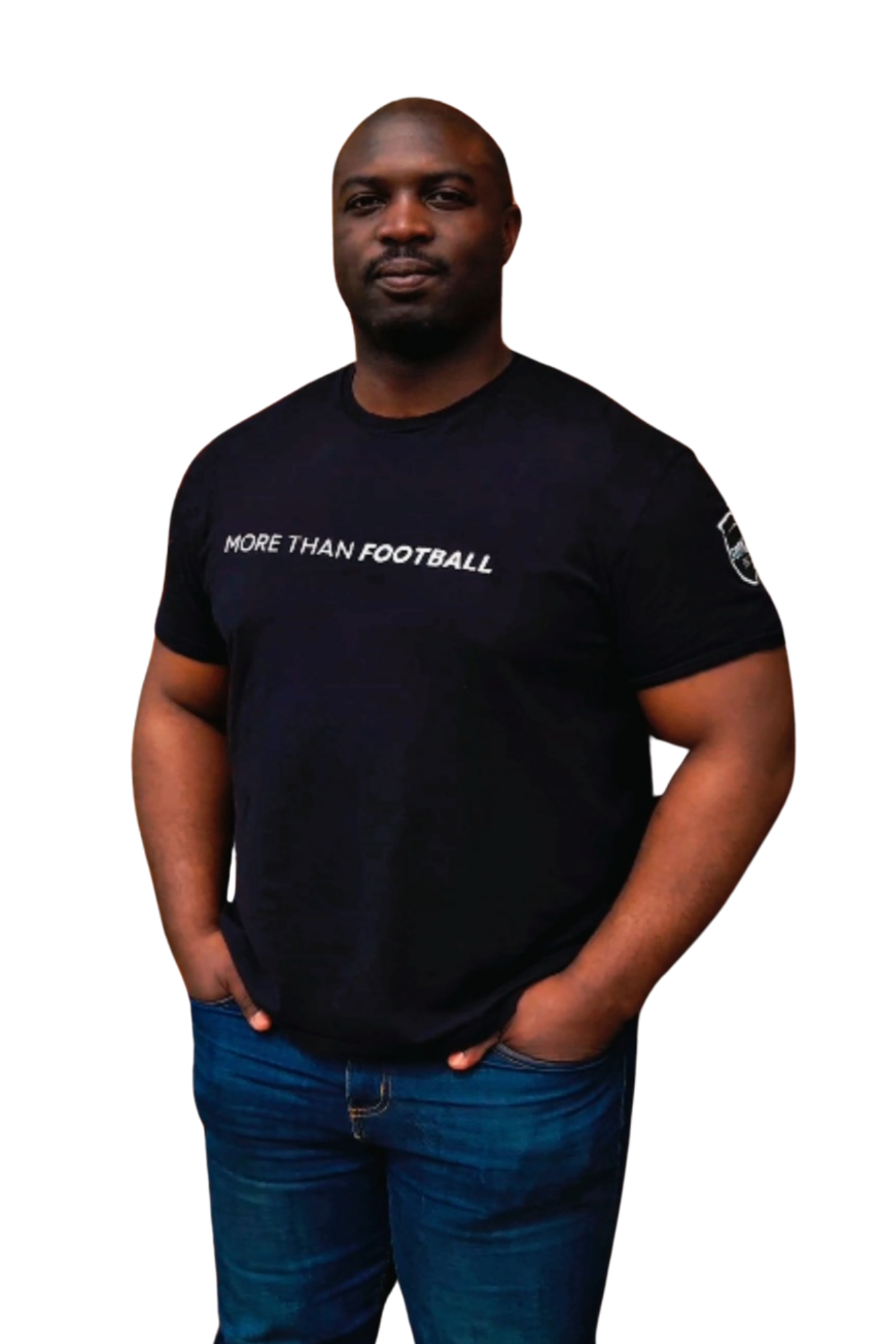 A person wearing a black t-shirt with white text that says 'MORE THAN FOOTBALL', with dark blue jeans, standing against a black background.