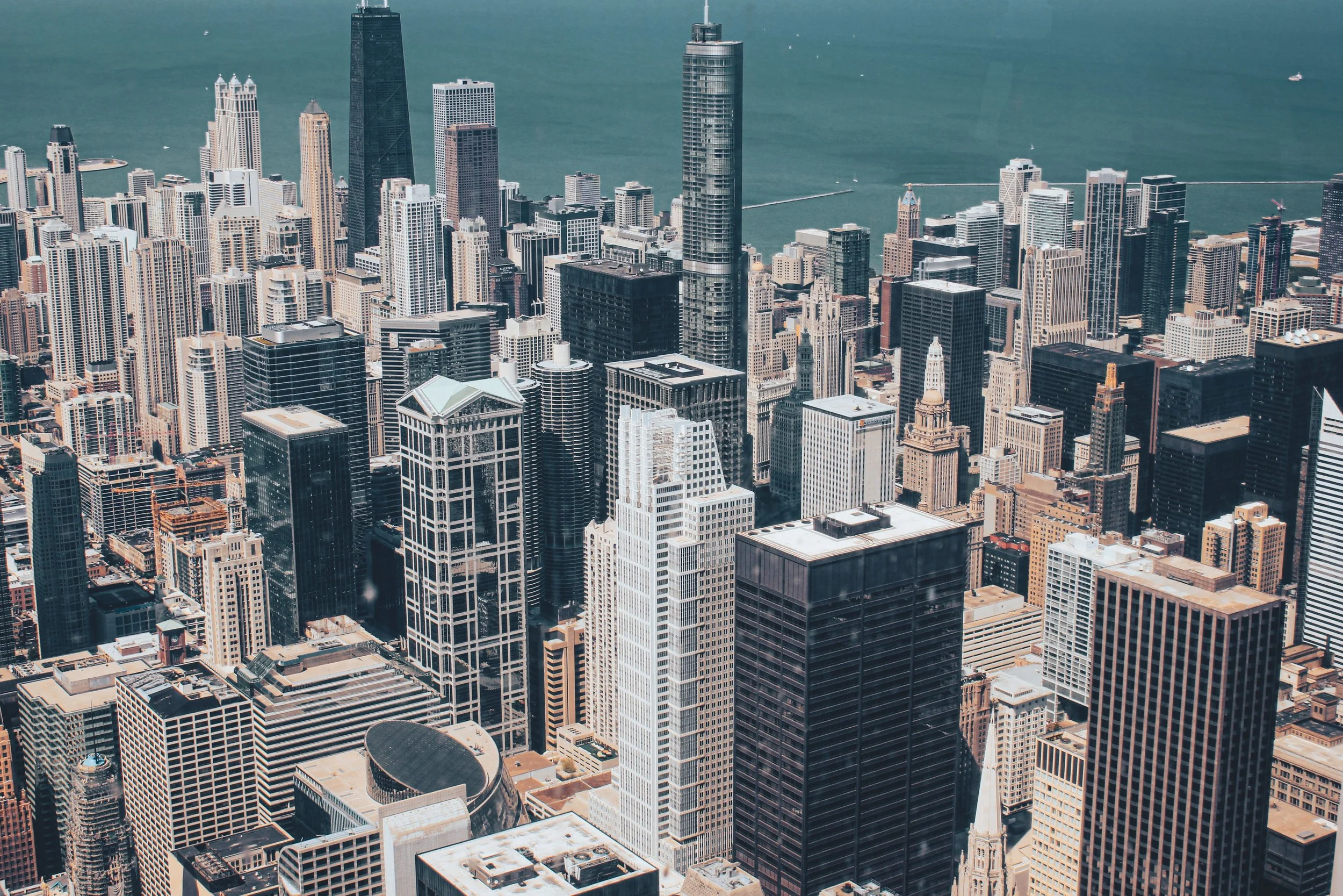 Aerial view of a dense city skyline featuring tall skyscrapers with Lake Michigan in the background.