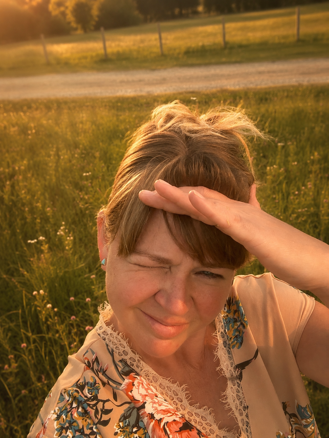 Natalie Winters, founder of Humble Pie Promotions., in a grassy field during sunset, touching her forehead with her hand.