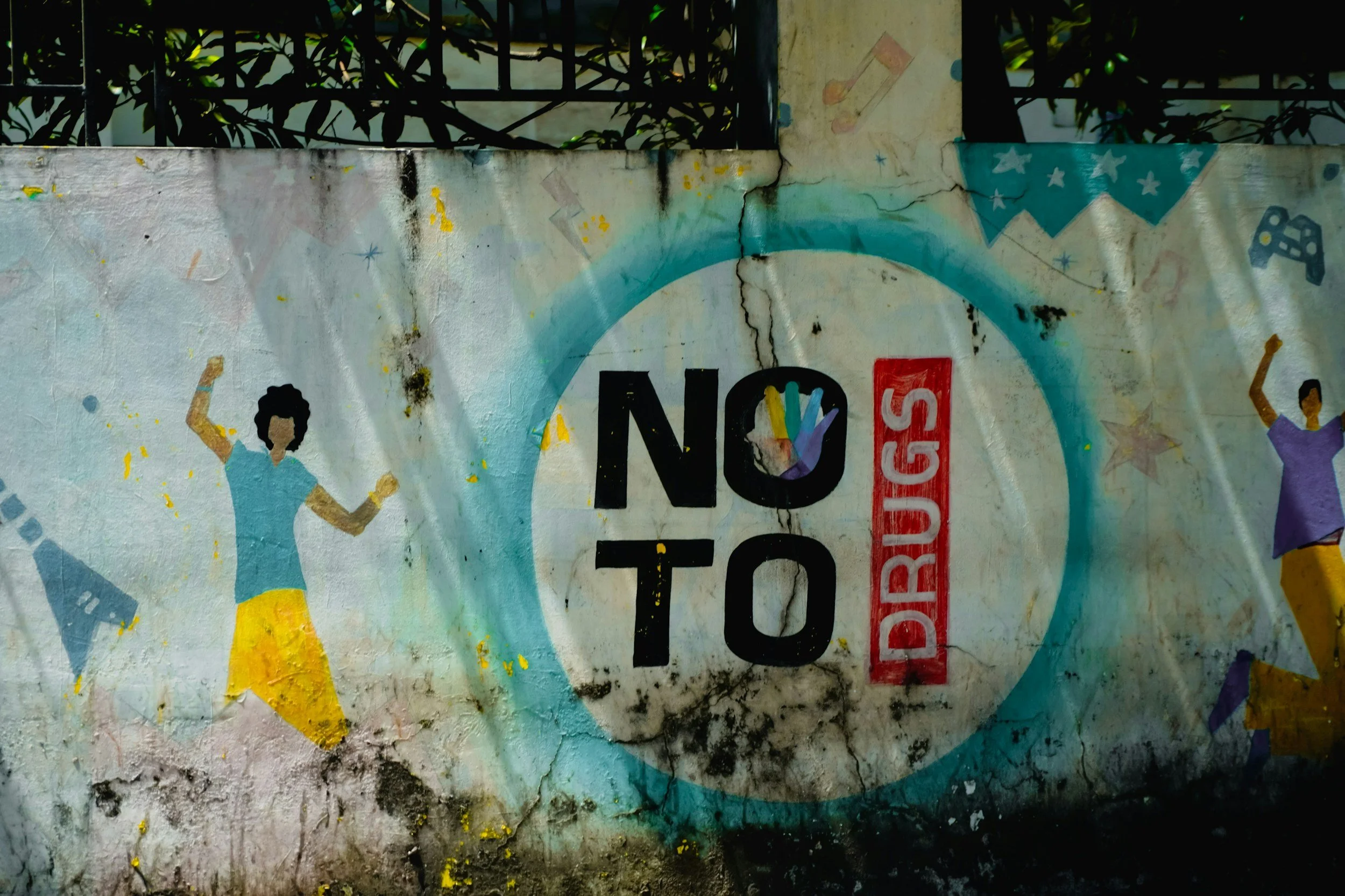 Painted wall with illustrations of women dancing, stars, a dice, and a pair of hands, along with partially visible words 'NO' and 'DURING STOP.' The wall appears aged with visible cracks and black stains.