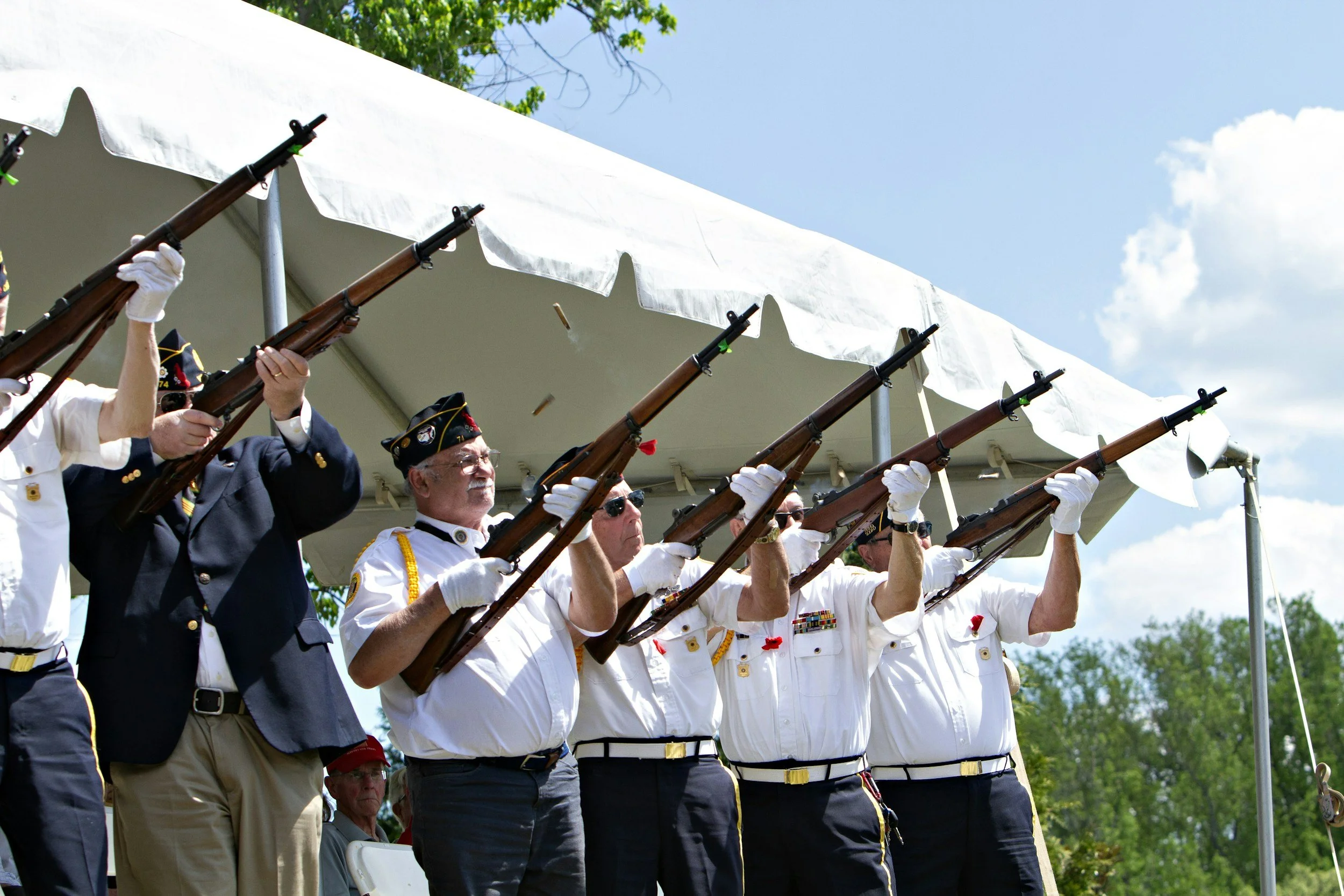 Veterans participating in a memorial ceremony, standing in uniform and firing rifles in tribute.