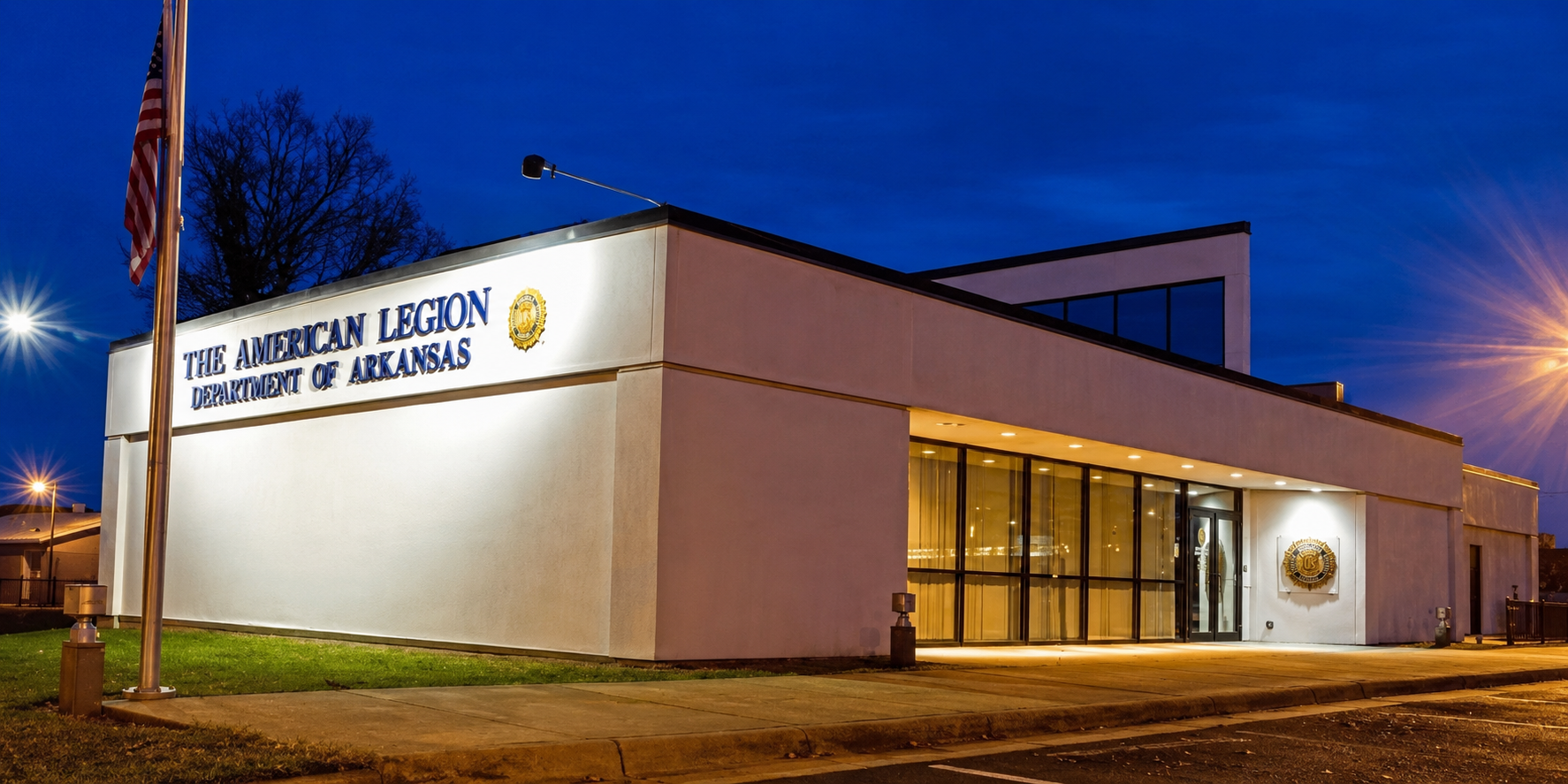 Night view of the American Legion building in Arkansas, illuminated sign and flag in foreground.