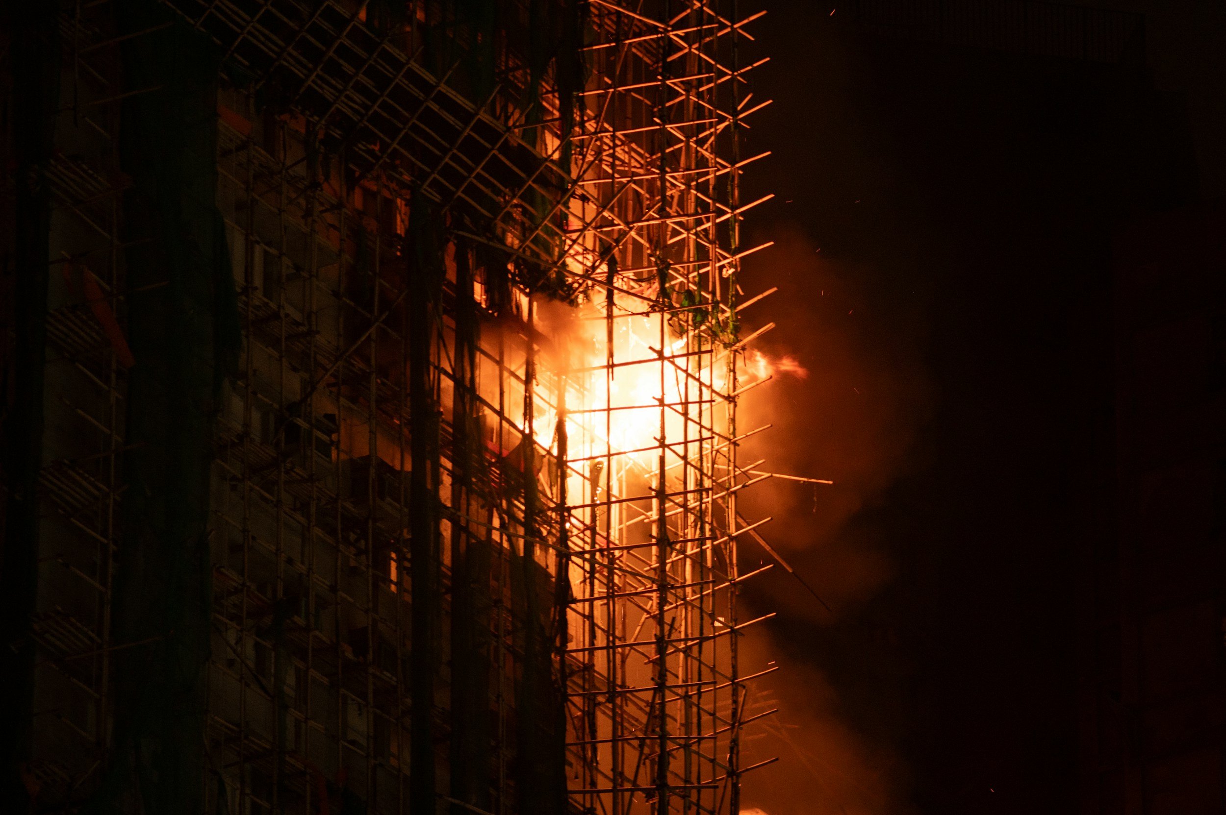 Baugerüst auf einer Baustelle im Brand, Flammen und Rauch bei Nacht.