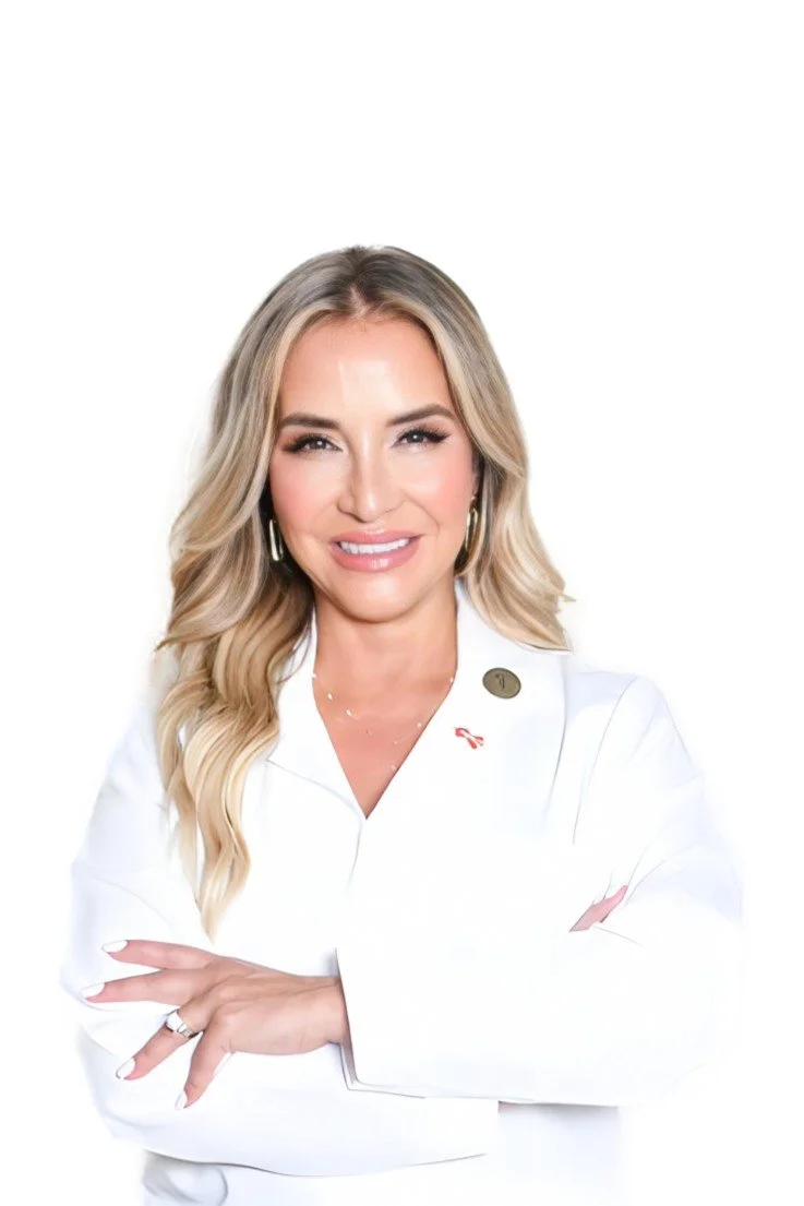 A woman with long blonde hair, smiling, wearing a white coat with a pin and a ribbon pin, standing with arms crossed against a plain white background.