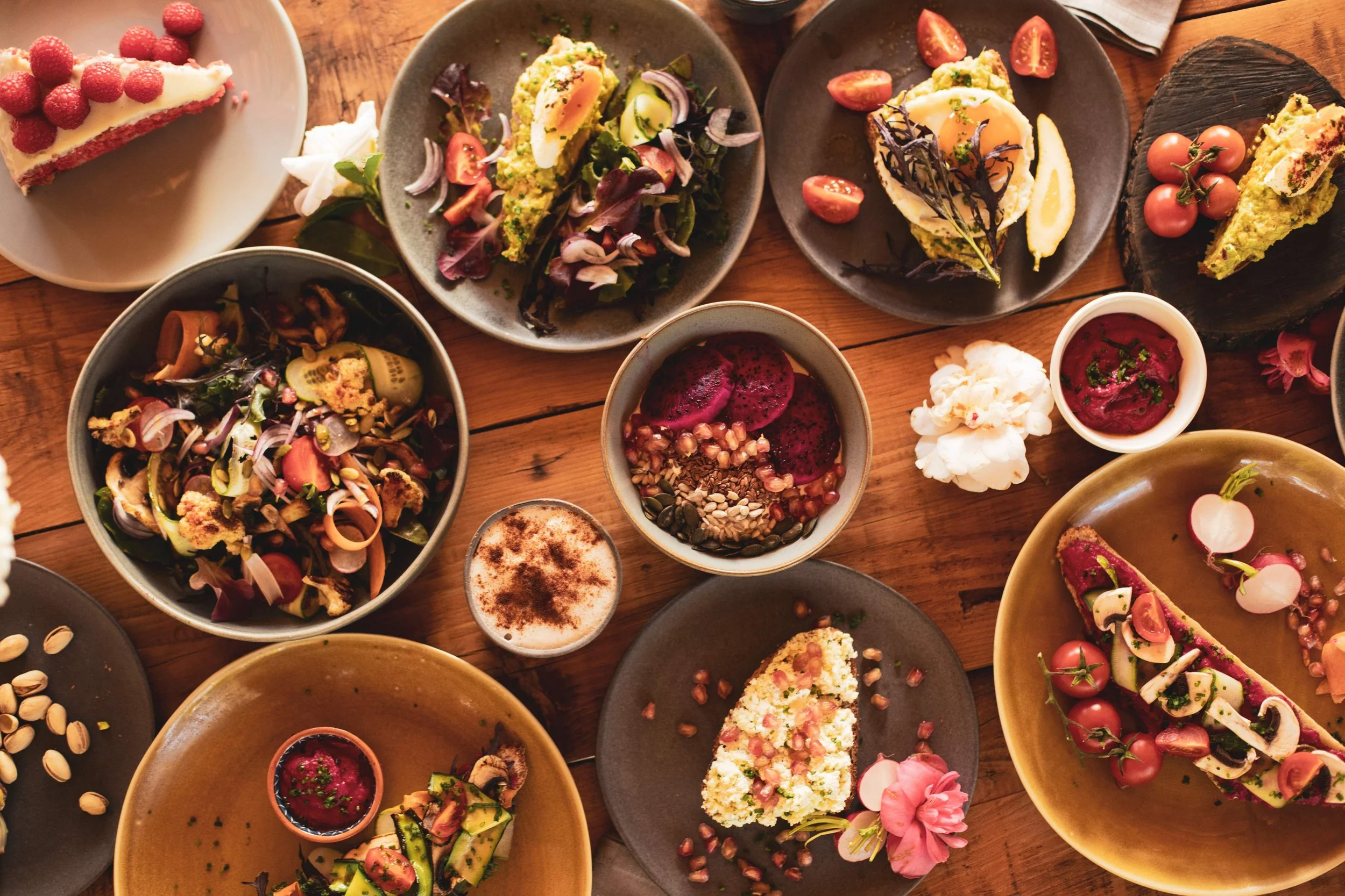 A variety of dishes on a wooden table in Portugal, including salads, slices of cake with berries, cherry tomatoes, and small bowls of sauces or dips.