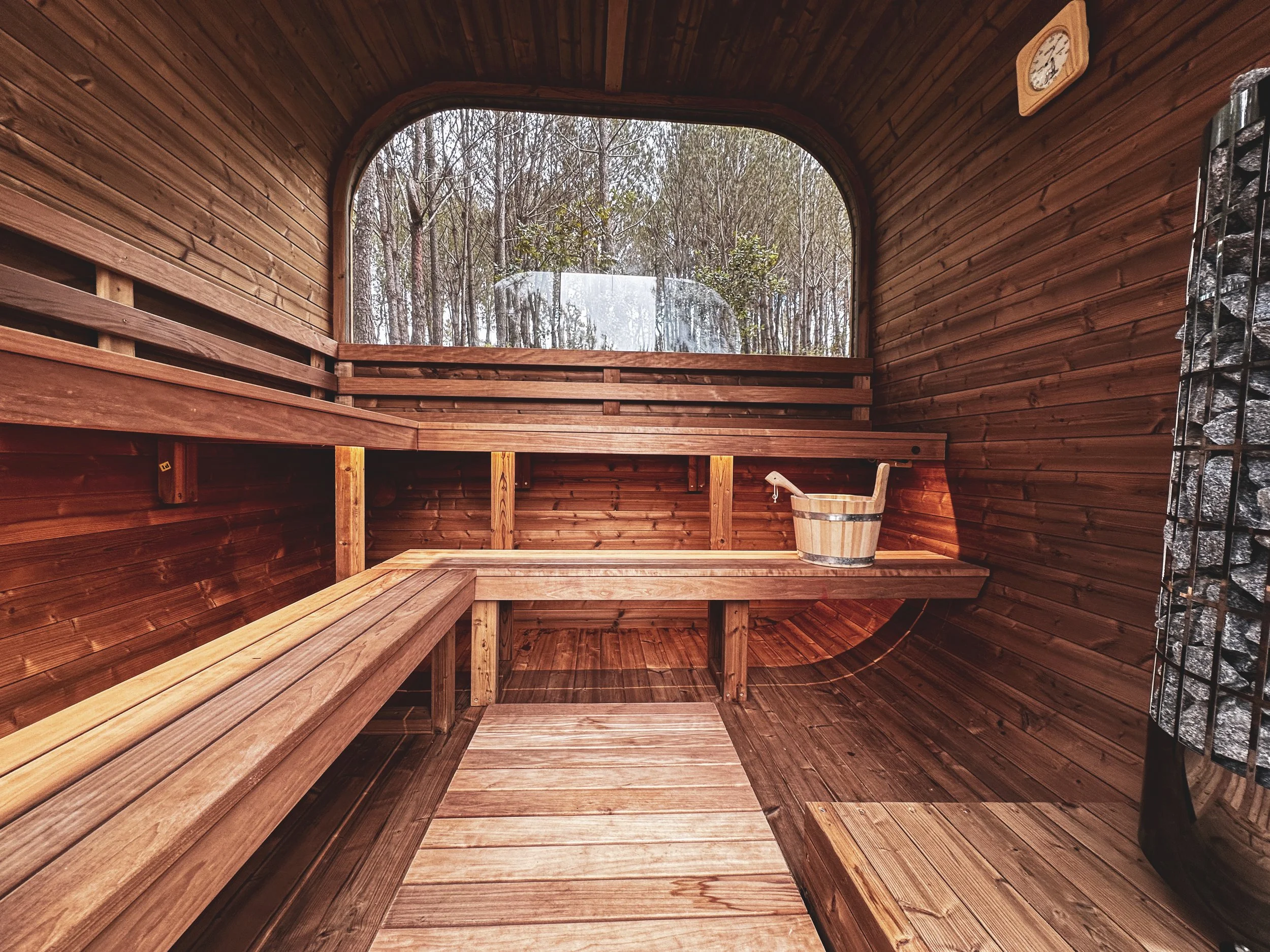 Inside a wooden sauna at Quinta Camarena Alentejo, Portugal with benches, a small bucket, and a window looking out to trees.