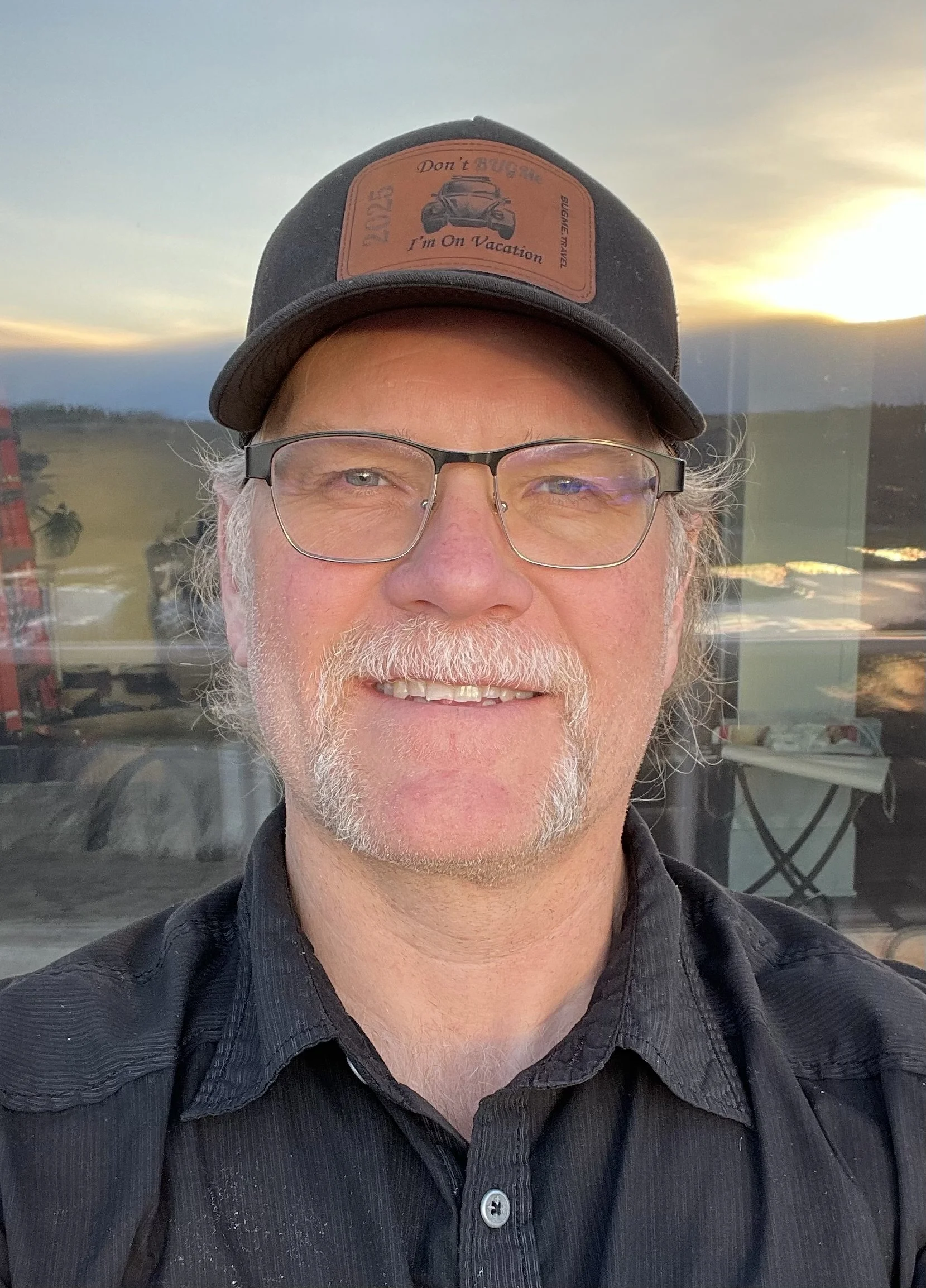 Ray Bretzloff, author of Business After Capitalism, wearing a baseball cap with patch saying "Don't BUGMe I'm On Vacation".