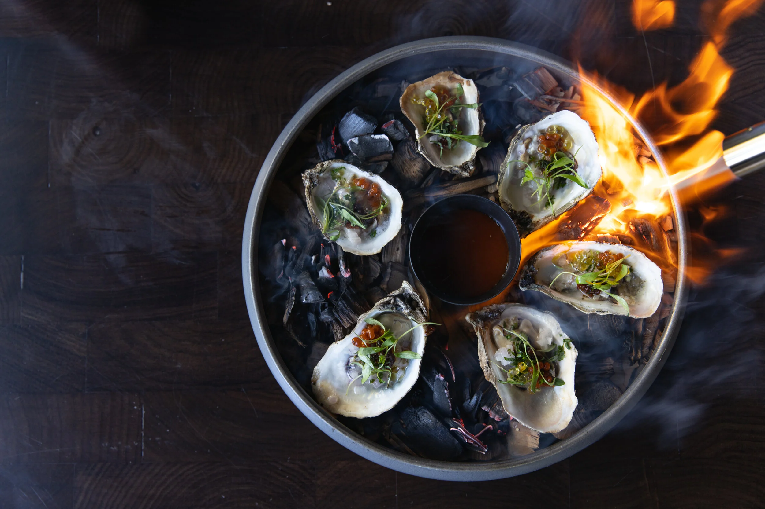 Oysters topped with herbs and sauce, being cooked on an open flame grill.