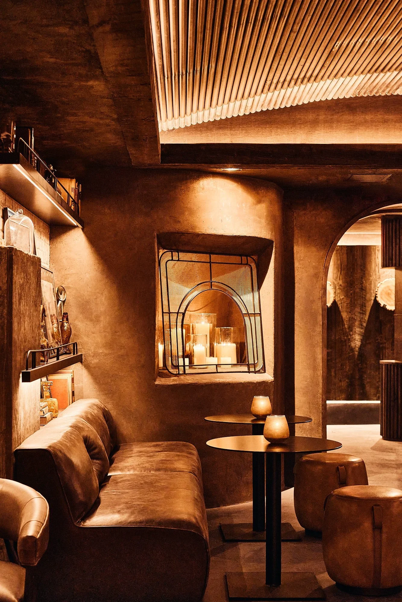 Cozy, warmly lit cafe interior with brown leather couches, small round tables with candles, wooden accents, and dim lighting.
