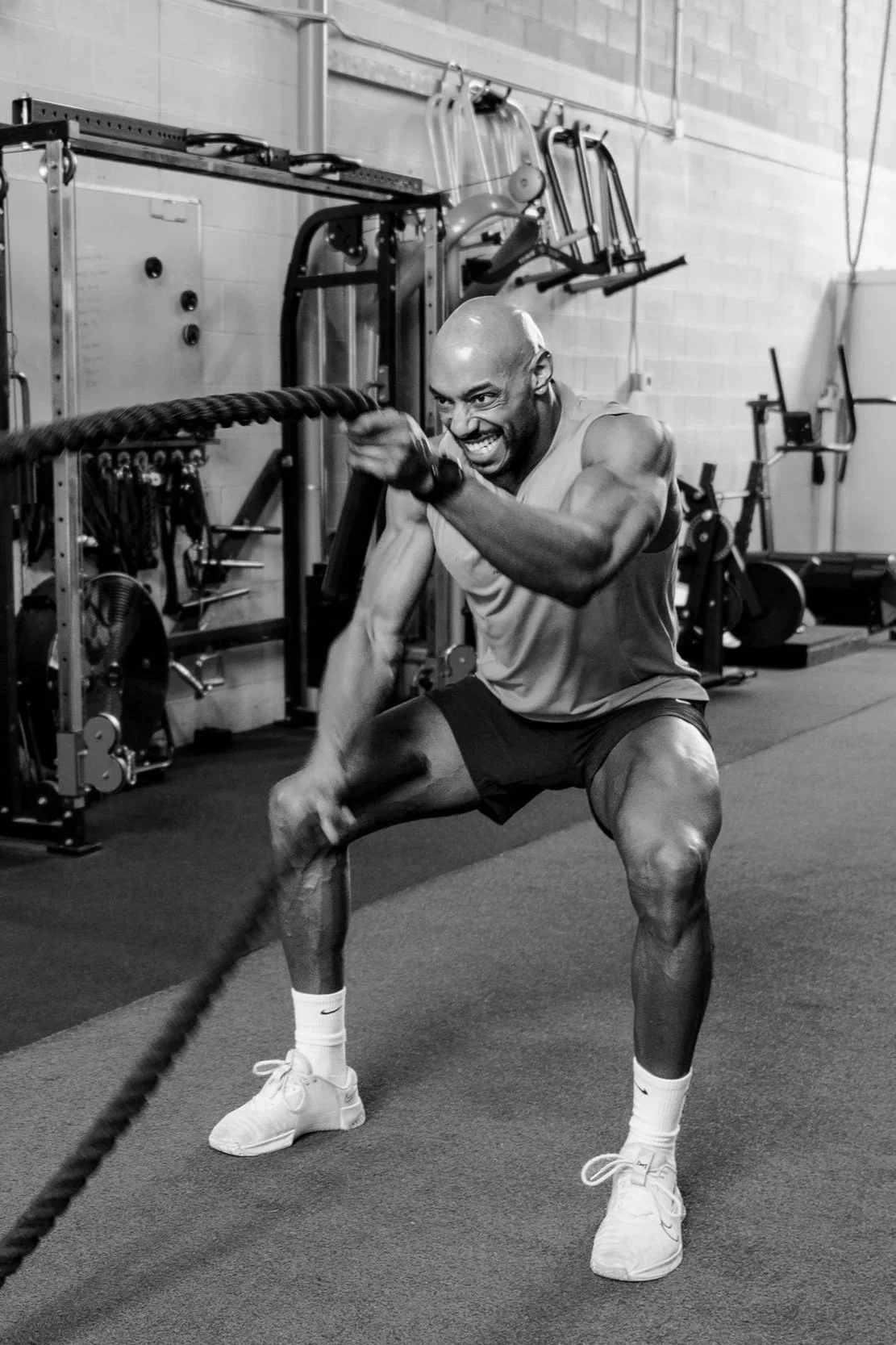 A muscular man wrestling with battle ropes in a gym.