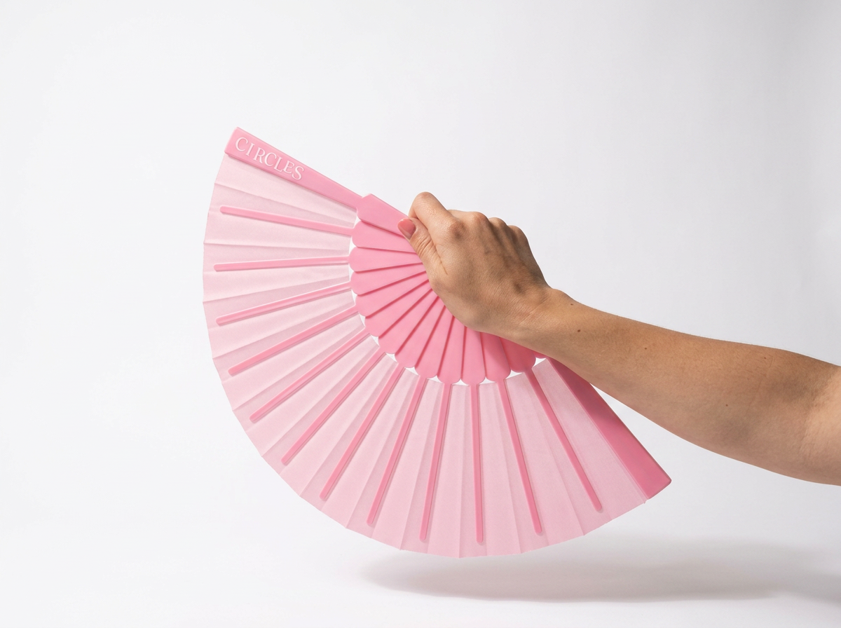A person holding a pink fan with the word "CIRCLES" written on it, partially unfolded, against a white background.
