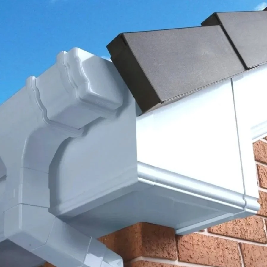 Close-up of a house's downpipe, soffit, facia and dry verge against a blue sky and brick wall.