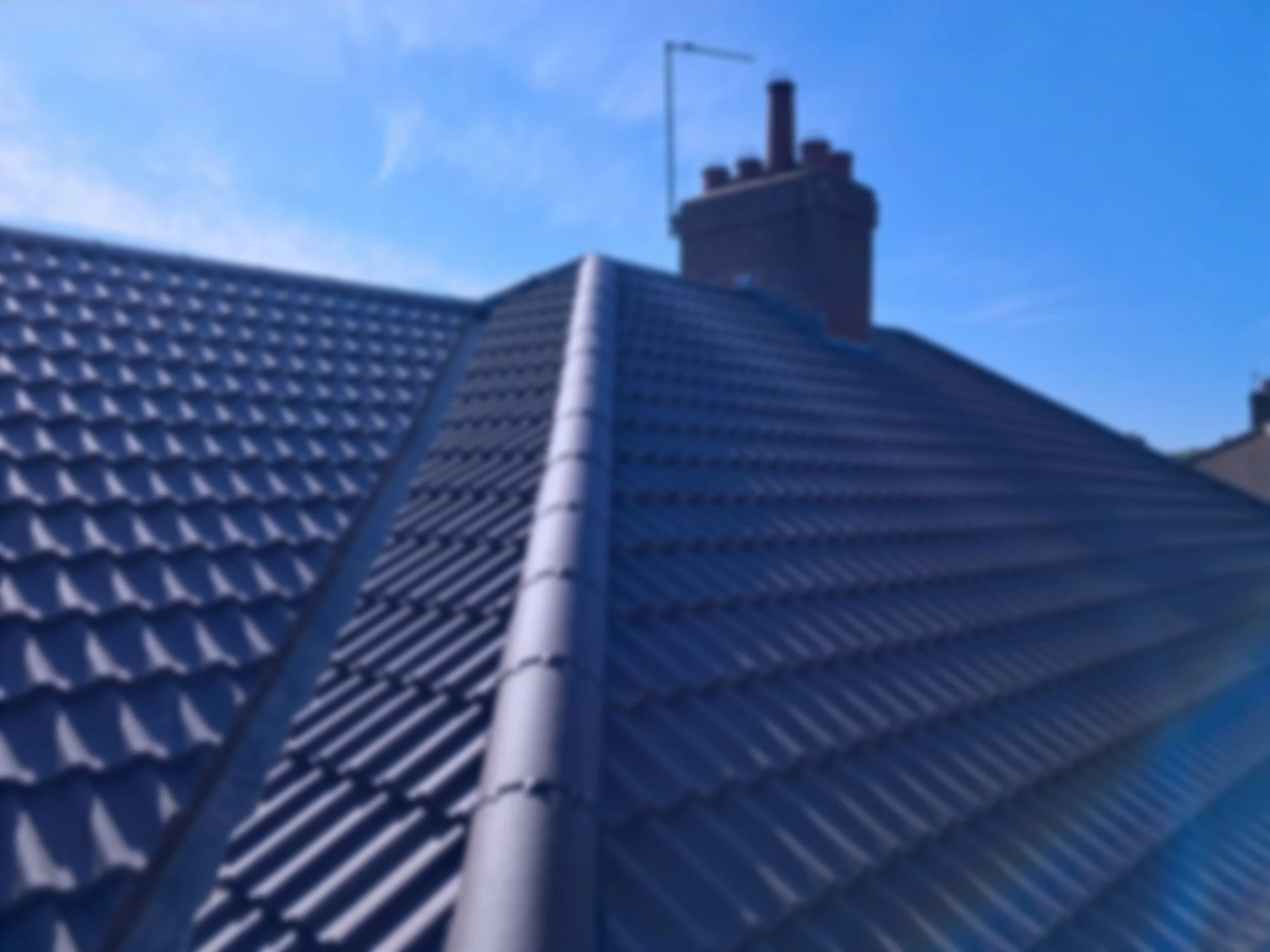 A rooftop with marley roof tiles and a brick chimney against a clear blue sky.