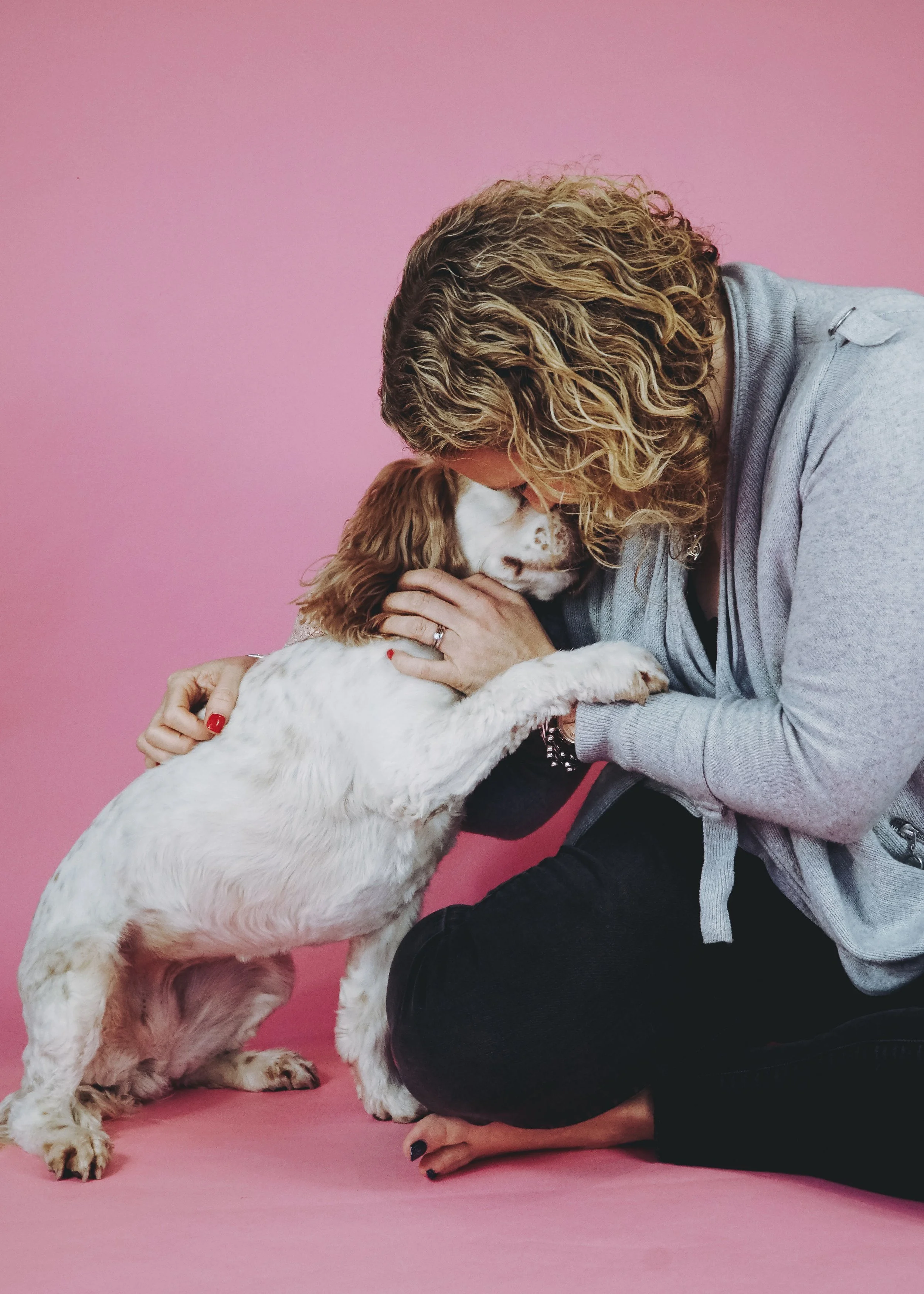 Person with curly hair hugging an English Springer Spaniel dog against a pink background.
